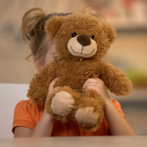 Adorable smiling girl holding brown teddy bear, joyful kid, happy childhood ostéopathie et émotions